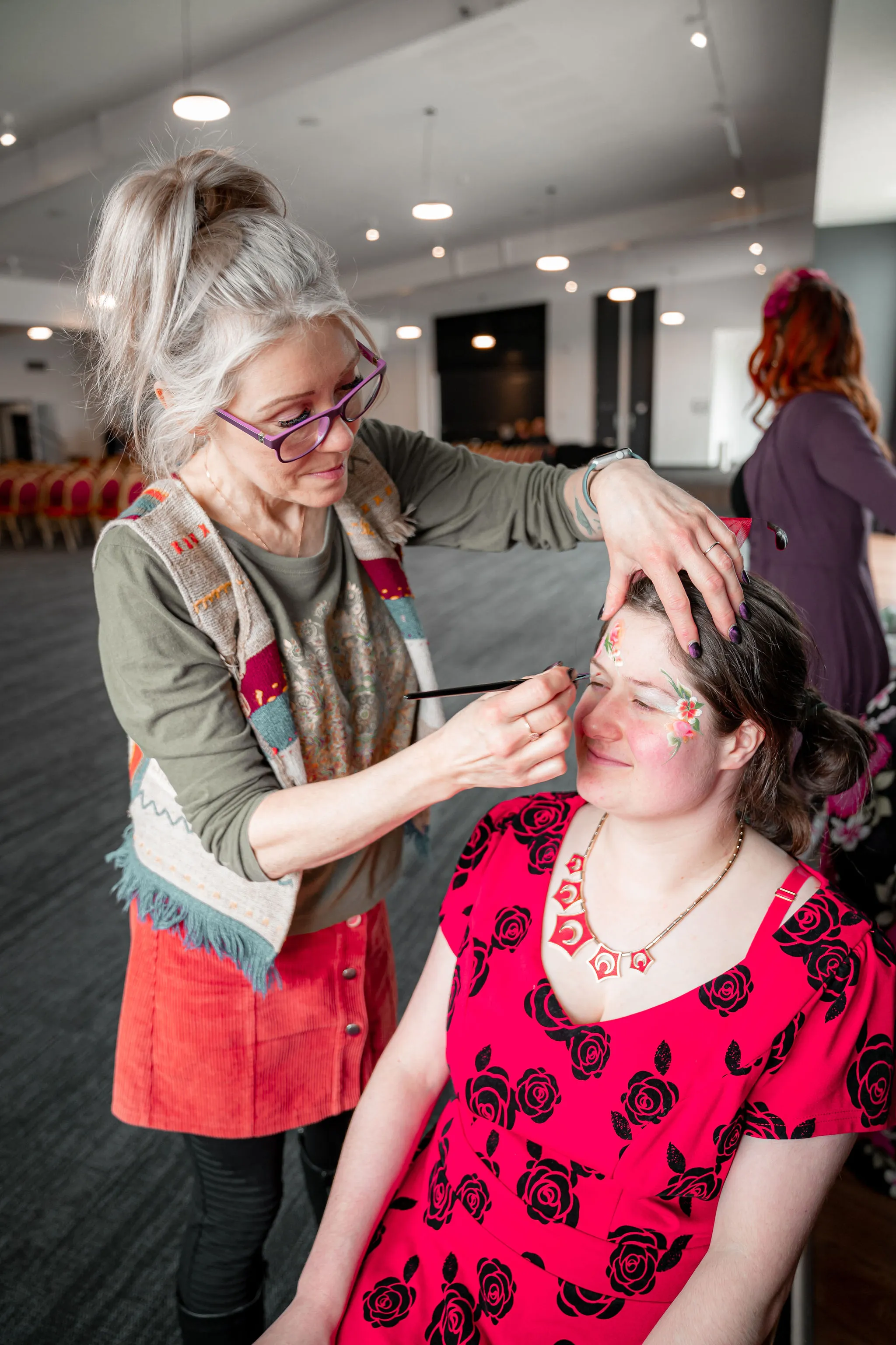 A volunteer painting a floral pattern on a participant's face.