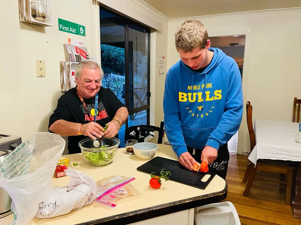 A resident and a support worker preparing dinner together in the kitchen.