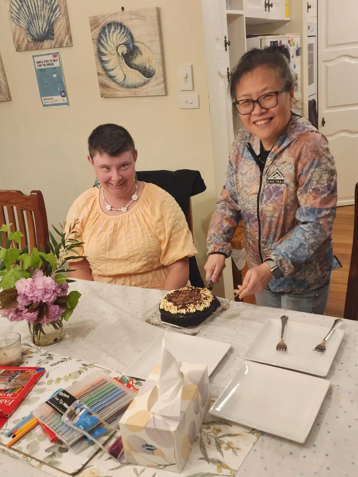A resident and her support worker sharing cake at the kitchen table.