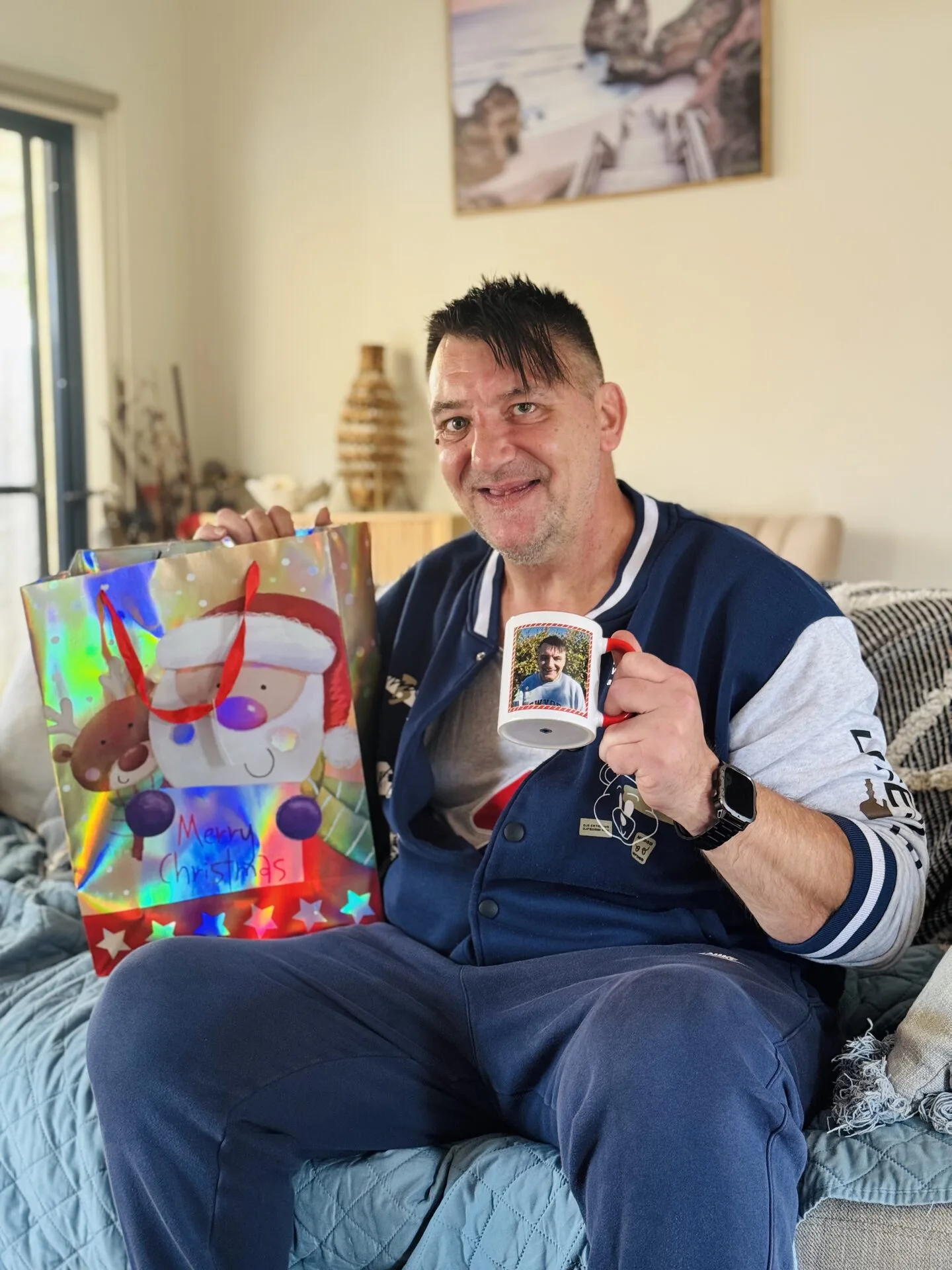 A resident on his sofa, holding a Christmas gift bag and a mug.