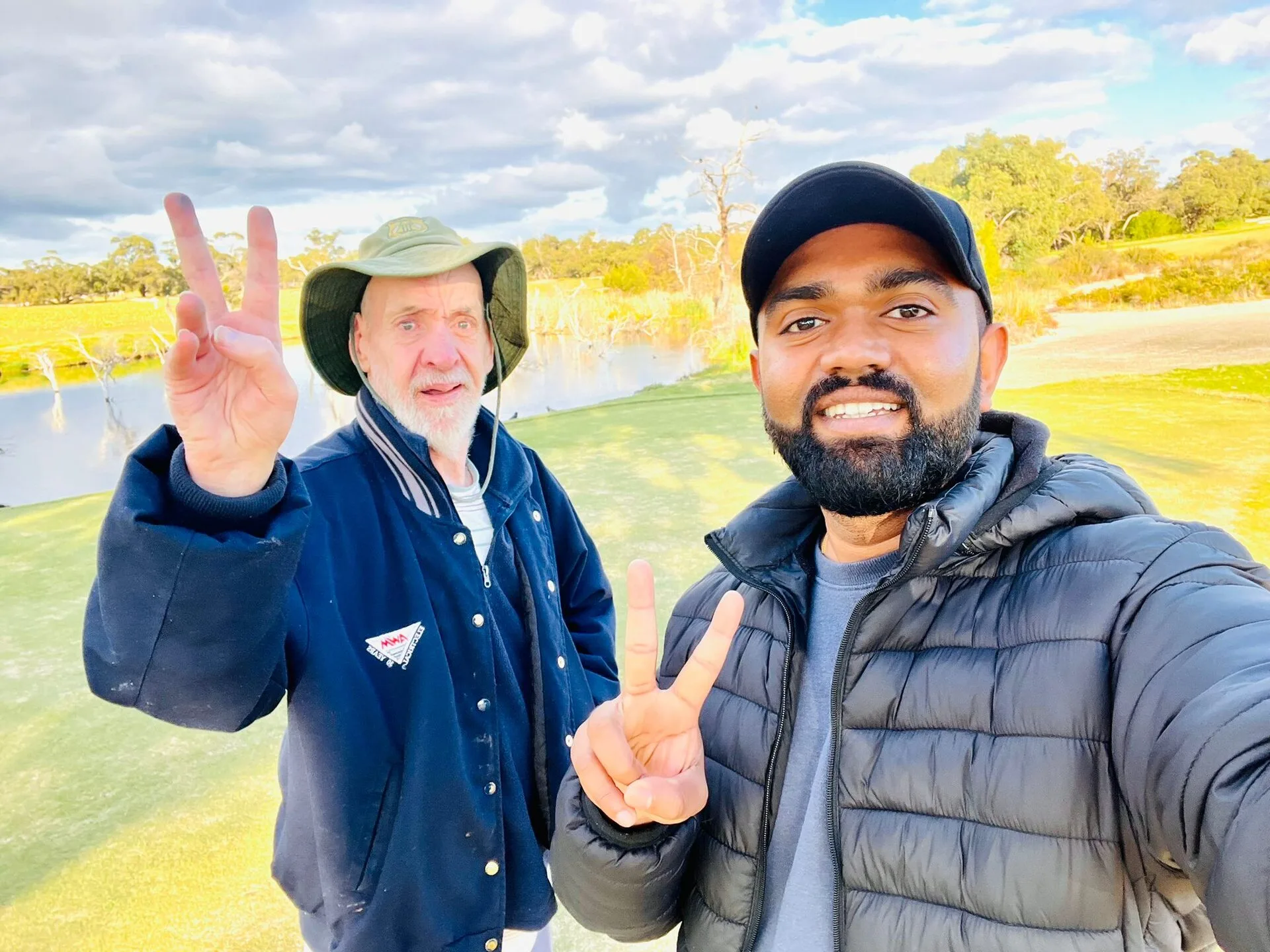 A resident and staff member outdoors by the water, making peace signs.